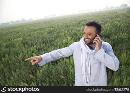 Indian man in a field pointing away while on a call