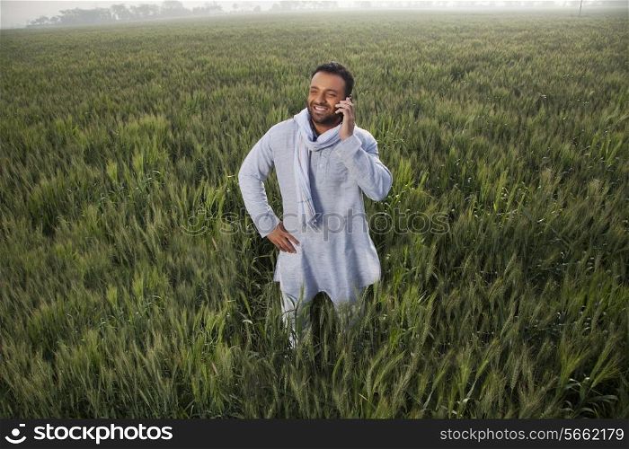 Indian man in a field talking on phone with hand on hip