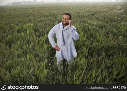 Indian man in a field talking on phone with hand on hip