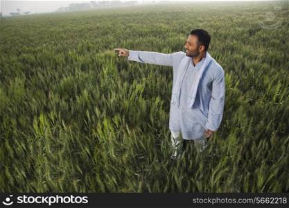 Indian man pointing at something while standing in a field