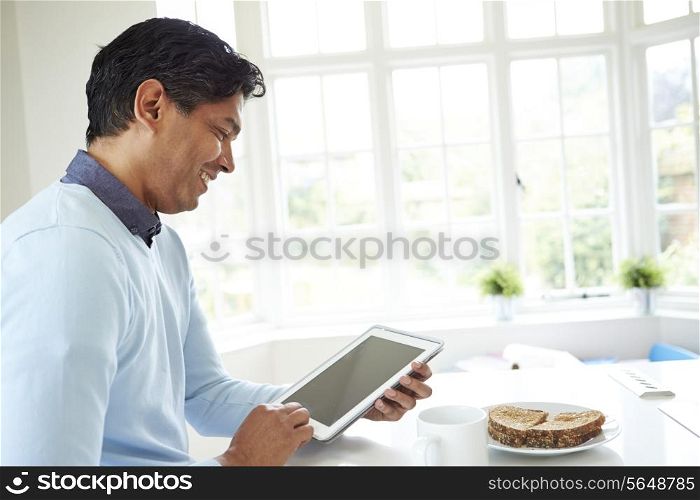 Indian Man Using Digital Tablet Whilst Eating Breakfast