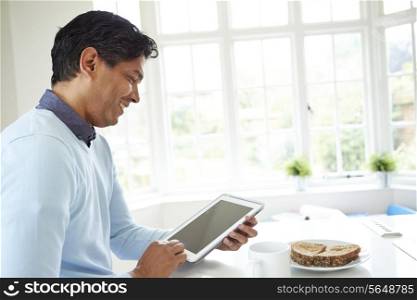 Indian Man Using Digital Tablet Whilst Eating Breakfast