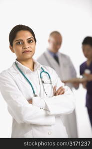 Indian mid adult woman doctor standing with medical staff in background.