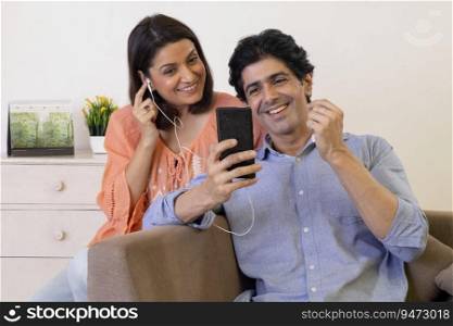 Indian middle age couple listening music on mobile through earphone at home
