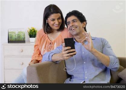 Indian middle age couple listening music on mobile through earphone at home