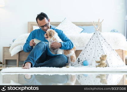 Indian middle aged man in traditional clothes working sitting on floor, relaxing playing with shih tzu dog puppy in bedroom at home. Pet friendly residence, lifestyle, pet and human bonding concept