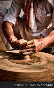 Indian potter at work: throwing the potter&rsquo;s wheel and shaping ceramic vessel and clay ware: pot, jar in pottery workshop. Experienced master. Handwork craft from Shilpagram, Udaipur, Rajasthan, India. Indian potter at work, Shilpagram, Udaipur, Rajasthan, India