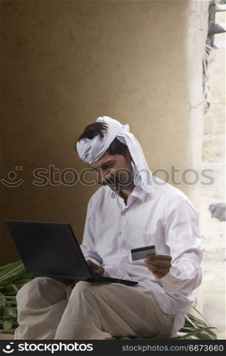 Indian rural man using laptop and holding credit card