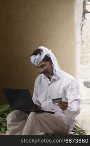 Indian rural man using laptop and holding credit card