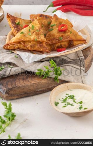 Indian samosas - fried or baked pastry with savoury filling, popular Indian snacks, served with yogurt sauce in areca leaf dishes with spices on kitchen countertop