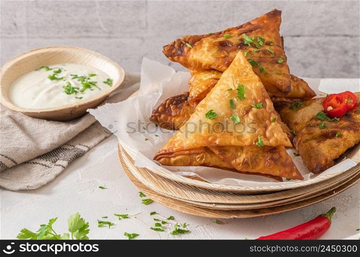 Indian samosas - fried or baked pastry with savoury filling, popular Indian snacks, served with yogurt sauce in areca leaf dishes with spices on kitchen countertop