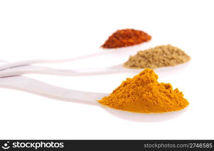 indian spices in measuring spoons (curcuma, coriander, red pepper flakes) isolated on white background (shallow DOF, focus on first)