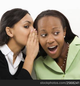 Indian young adult woman whispering in ear of mid-adult African-American woman.