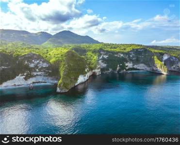 Indonesia. A large tropical island overgrown with jungle. Rocky shore of the ocean. The clouds on the blue sky. Aerial view. Rocky Shore of the Tropical Island and Clouds. Aerial View