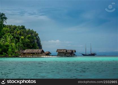 Indonesia. A tropical island covered with jungle. Cloudy evening. Yacht and huts on the water. Yacht and Huts on the Water