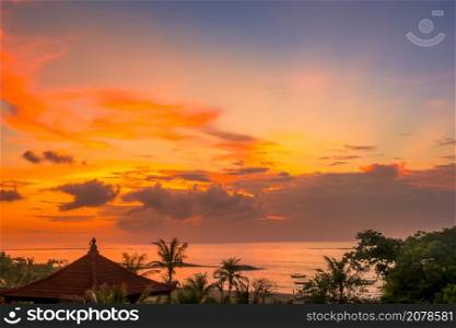 Indonesia. Bali island. Colorful sunset sky over the ocean and beach. Boats, palm trees and traditional roof. Sunset over the Beach of Bali