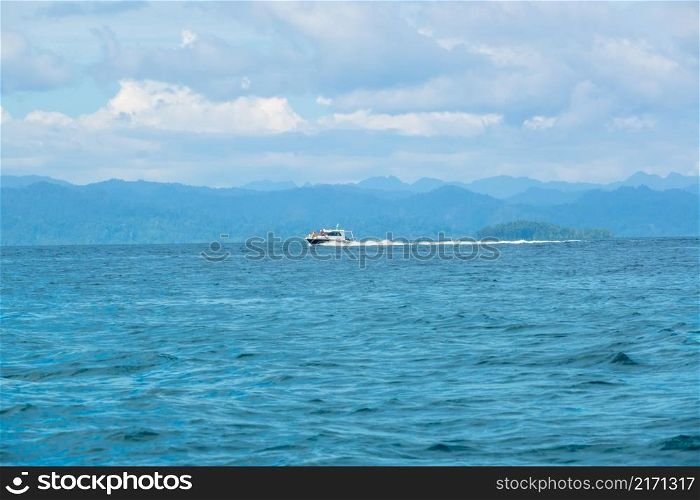 Indonesia. Cloudy sky and a motor yacht moving fast along a tropical coast. Motor Yacht Sails Fast Near a Tropical Island