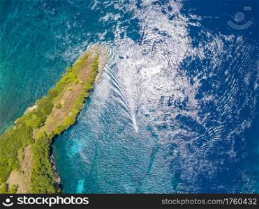Indonesia. Emerald surface of the ocean. A small boat trimaran near a tropical island, overgrown with jungle. Aerial view vertically down. Island in the Ocean and a Boat Trimaran. Aerial View