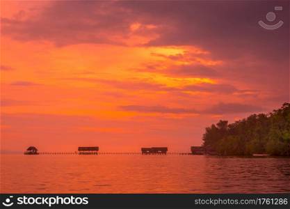 Indonesia. Raja Ampat archipelago. Coast of the island with a pier for boats. Calm ocean and orange sunset. Orange Sunset on a Tropical Island