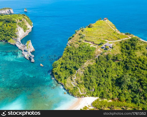 Indonesia. Rocky coast of a tropical island. Turquoise water and a small beach. Several huts on the top of the cliff and a staircase along the slope. Aerial view. Tropical Coast and Huts on the Top of the Cliff. Aerial View