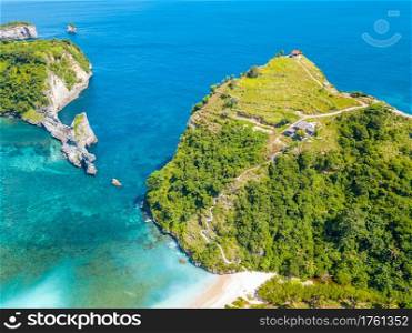 Indonesia. Rocky coast of a tropical island. Turquoise water and a small beach. Several huts on the top of the cliff and a staircase along the slope. Aerial view. Tropical Coast and Huts on the Top of the Cliff. Aerial View