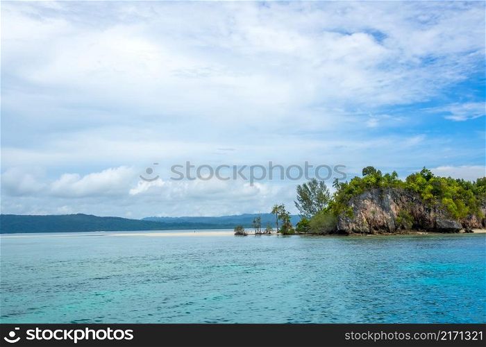 Indonesian island in the Raja Ampat archipelago. Sandy spit on the coast of a tropical island. Lonely human figure. The hut is hiding behind the trees. Sandbar Near a Tropical Island and Jungle in the Background