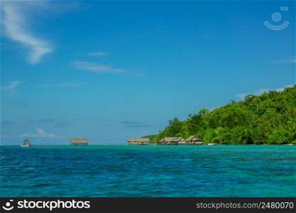 Indonesian islands. Blue sky. Coast of the ocean and the jungle. Huts on stilts in the water. Island Covered with Jungle and Huts on the Water