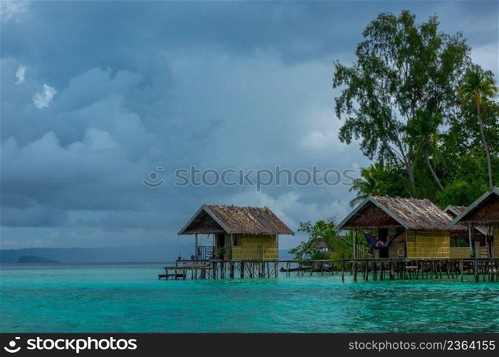 Indonesian islands. Cloudy evening. Coast of the ocean and the jungle. Huts on stilts in the water. Cloudy Evening and Huts on the Water
