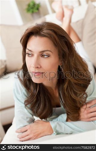 Indoor portrait of a beautiful thoughtful young brunette woman in her thirties laying on a sofa or settee at home