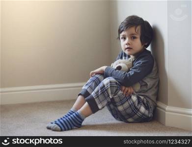 Indoor protrait of happy boy with bright light morning background, Hight key light of child sitting on carpet floor playing with teddy bear and looking at camera with smiling face,