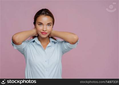Indoor shot of brunette woman presses hair, has makeup, well cared complexion and fresh healthy skin, dressed in shirt, going to have walk with boyfriend, isolated over purple wall, copy space aside