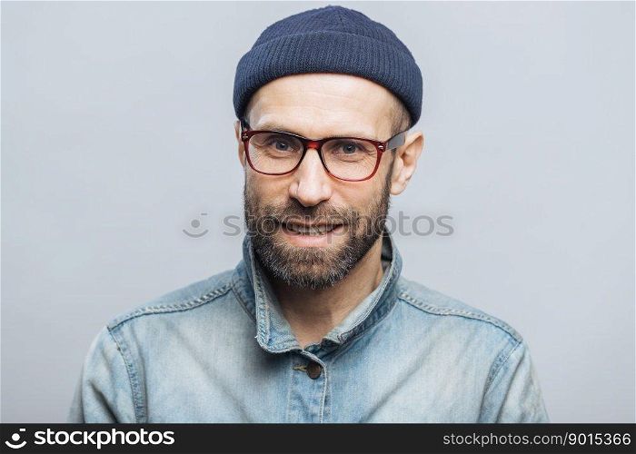 Indoor shot of handsome unshaven male with satisfied expression, rejoices achieving success at work, looks happily through spectacles, isolated over white background. Smiling bearded man indoor