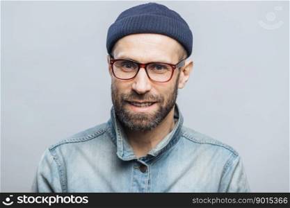 Indoor shot of handsome unshaven male with satisfied expression, rejoices achieving success at work, looks happily through spectacles, isolated over white background. Smiling bearded man indoor