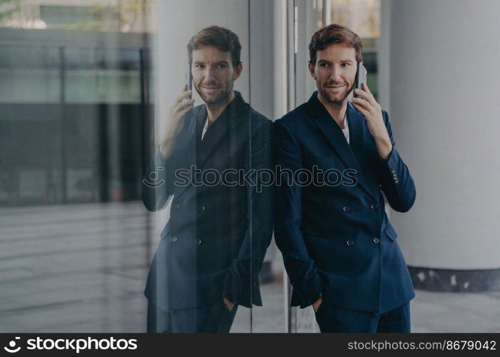 Indoor shot of thoughtful unshaven man employee uses mobile phone for communication arranges meeting with partner poses in modern office building dressed in formal wear. Distant conversation. Indoor shot of thoughtful unshaven man employee uses mobile phone for communication