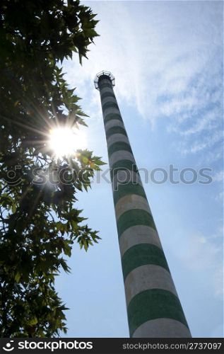 Industrial chimney and green tree. Sunlight