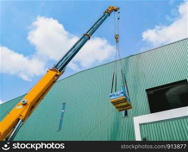 Industrial Crane operating and lifting a machine part against sunlight and blue sky