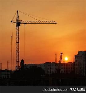 Industrial cranes over orange sunset with red sun