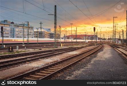 Industrial landscape. Railway Station in Nuremberg, Germany. Railroad with high speed train in motion at colorful sunset on the background of beautiful sky and city buildings.