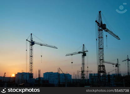 Industrial landscape with silhouettes of cranes on the sunset background