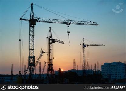 Industrial landscape with silhouettes of cranes on the sunset background