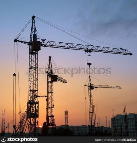 Industrial landscape with silhouettes of cranes on the sunset background