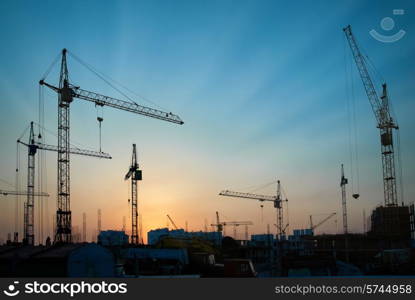 Industrial landscape with silhouettes of cranes on the sunset background