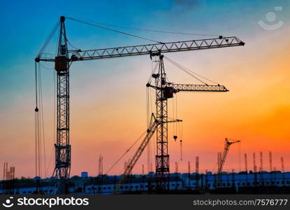 Industrial landscape with silhouettes of cranes on the sunset background