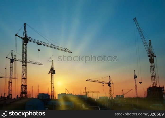 Industrial landscape with silhouettes of cranes over sunset