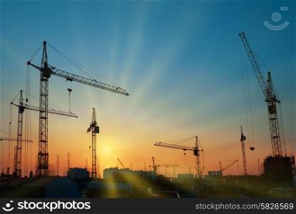 Industrial landscape with silhouettes of cranes over sunset