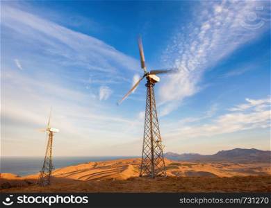 Industrial landscape with wind turbine generating electricity in mountains at sunset.