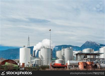 Industrial plant of a furniture factory with smoking chimneys against the backdrop of the Italian Alps
