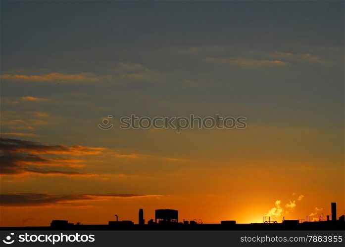 Industrial roof silhoutted against orange and purple clouds and dark sky at sunset.
