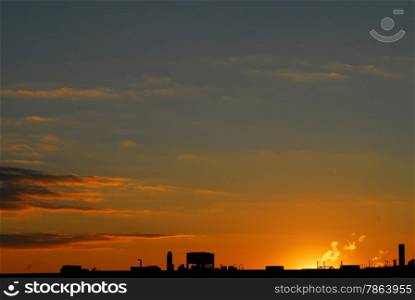 Industrial roof silhoutted against orange and purple clouds and dark sky at sunset.