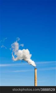 Industrial smokestack spewing white polluting smoke cloud vertically up and left into clear blue sky.